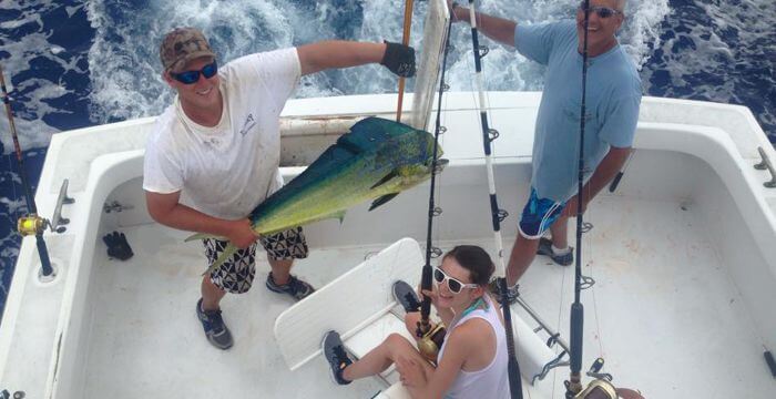 Charter mate holding mahi for a proud girl in the fighting chair that she just reeled in from the ocean on a faimly charter