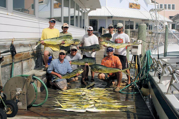 Group of a 8 guys holding mahi mahi with a pile of mahi mhi in front of them on the dock after an offshore charter.
